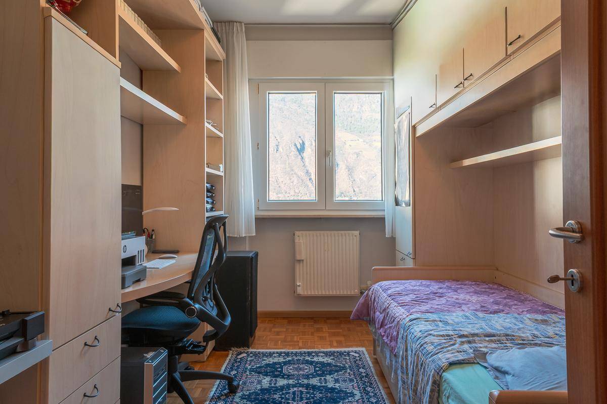 Kinderzimmer oder Büro mit Einzelbett, Schreibtisch und Einbauschränken.