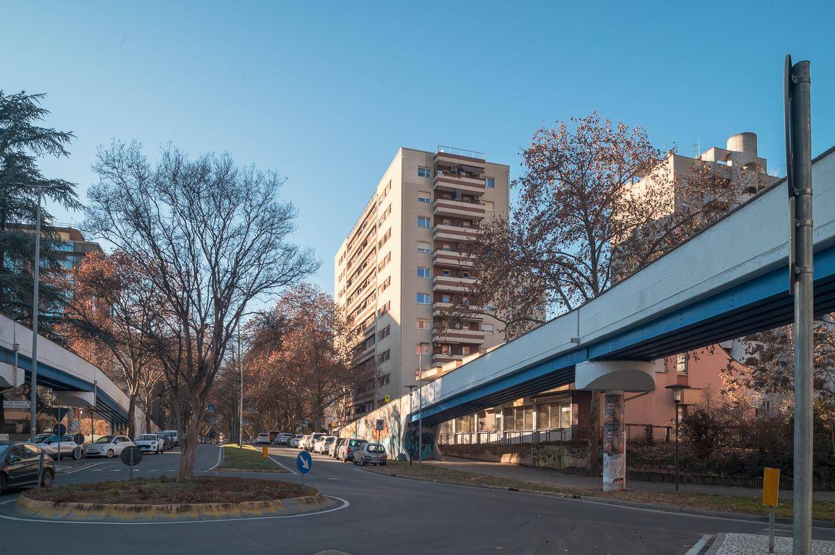 Stadtansicht mit Wohngebäuden, Bäumen und einer Fußgängerbrücke.