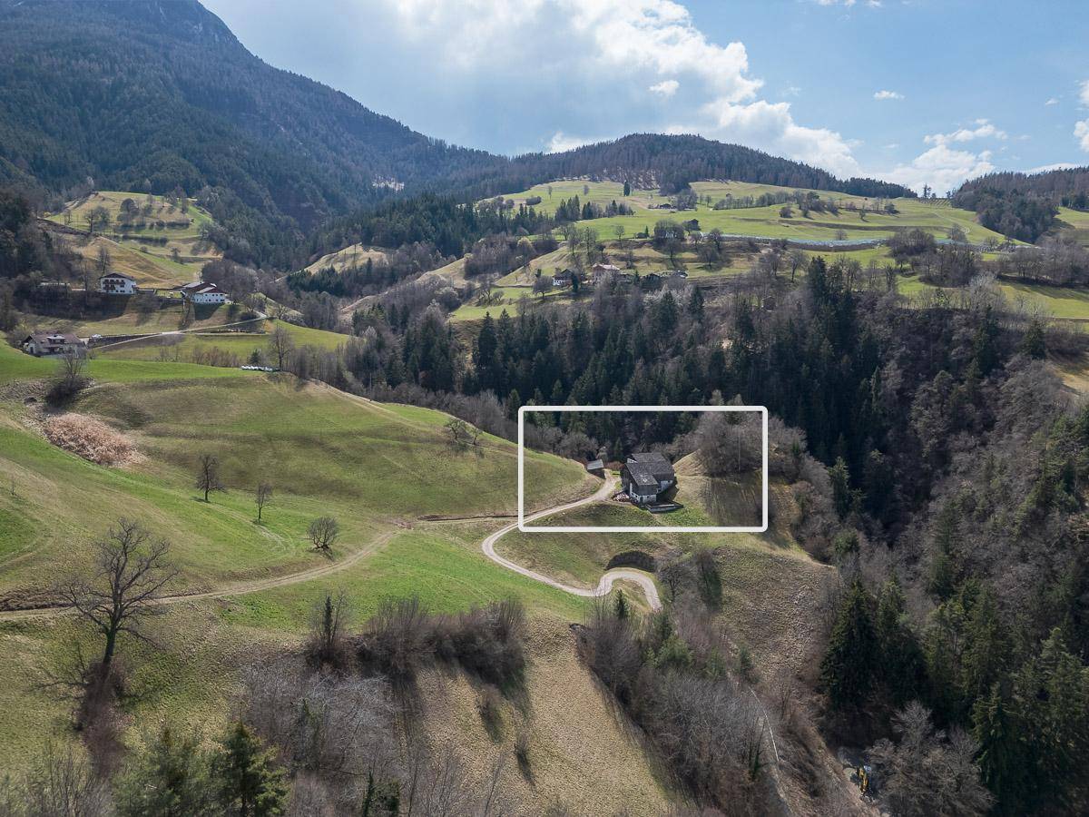 Luftaufnahme eines Anwesens in einer grünen Berglandschaft mit umgebenden Wäldern.