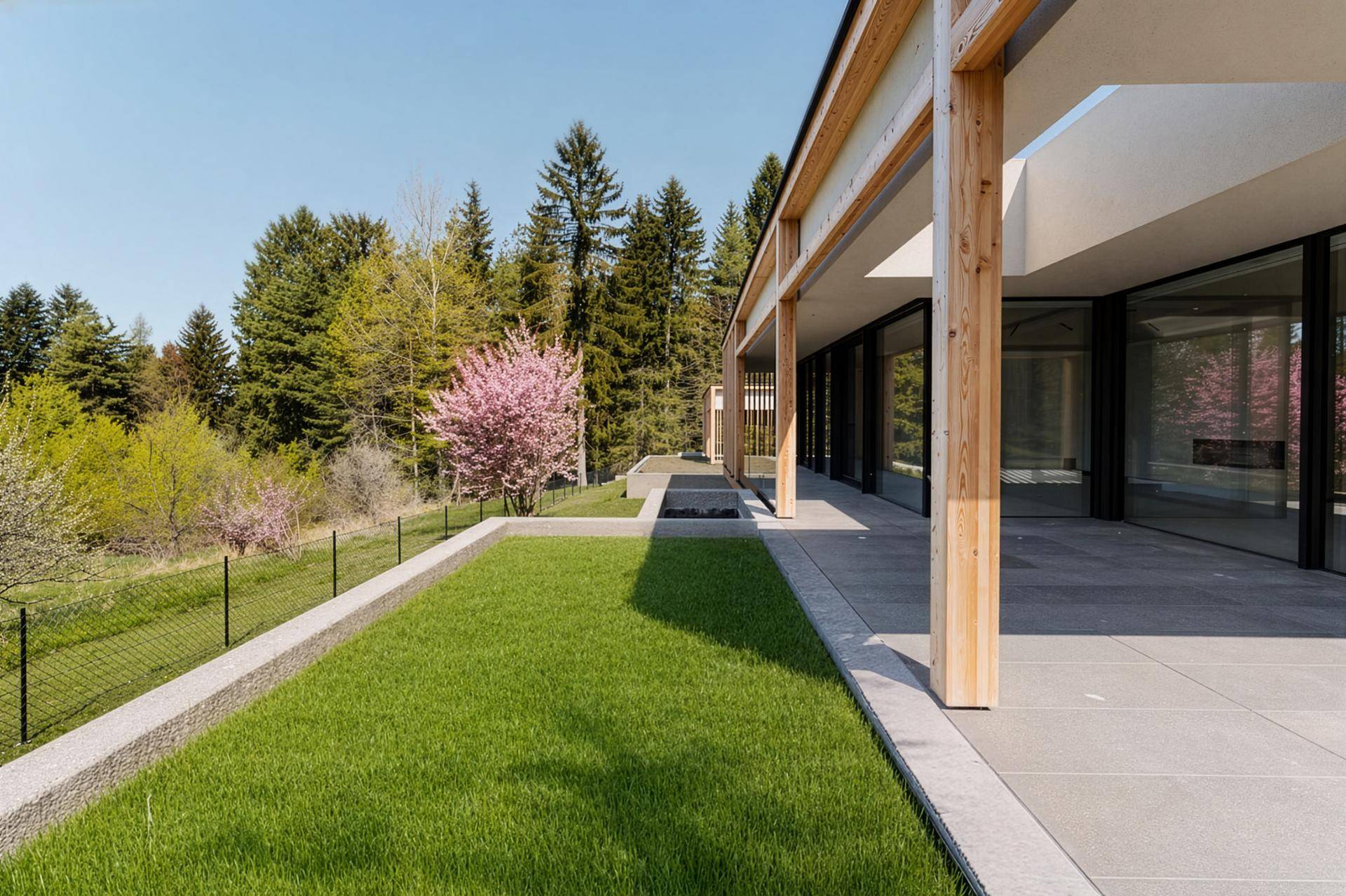 Gepflegte Rasenfläche neben der modernen Terrasse mit Blick auf die umliegende Natur.