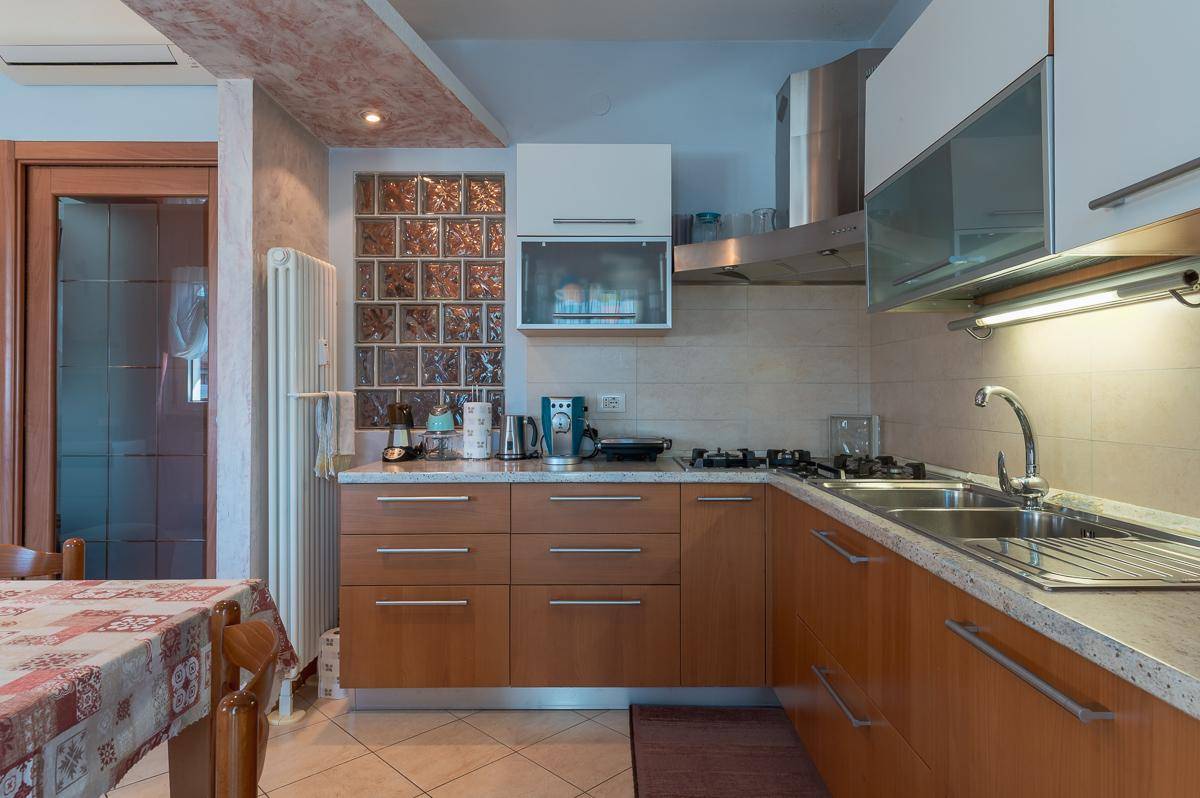 Detailansicht der Küche mit Gasherd, Spüle, Arbeitsfläche und Glasbausteinwand.