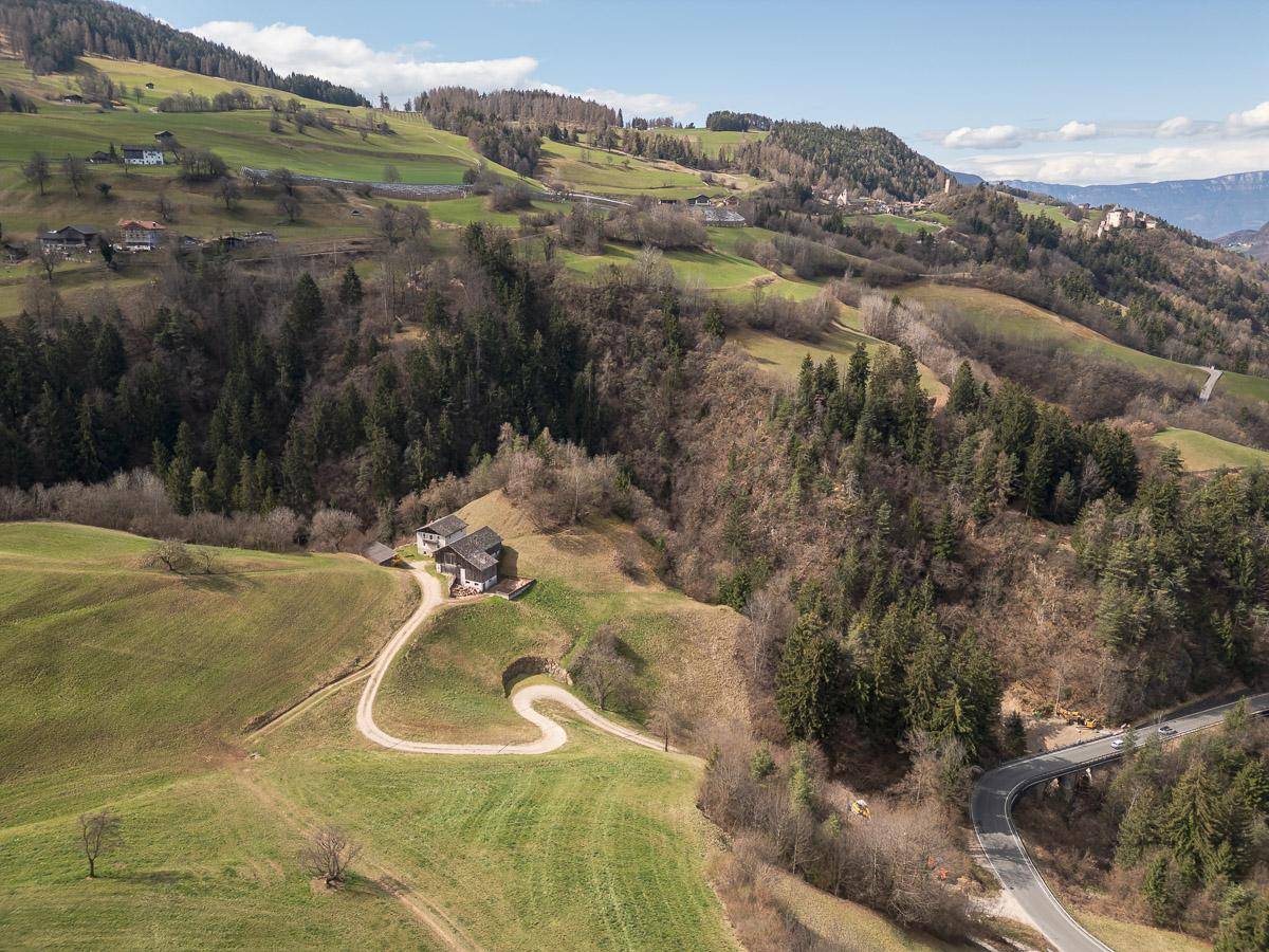 Weitläufige Luftaufnahme einer ländlichen Gegend mit Gebäuden, kurvigen Straßen und bewaldeten Hängen.