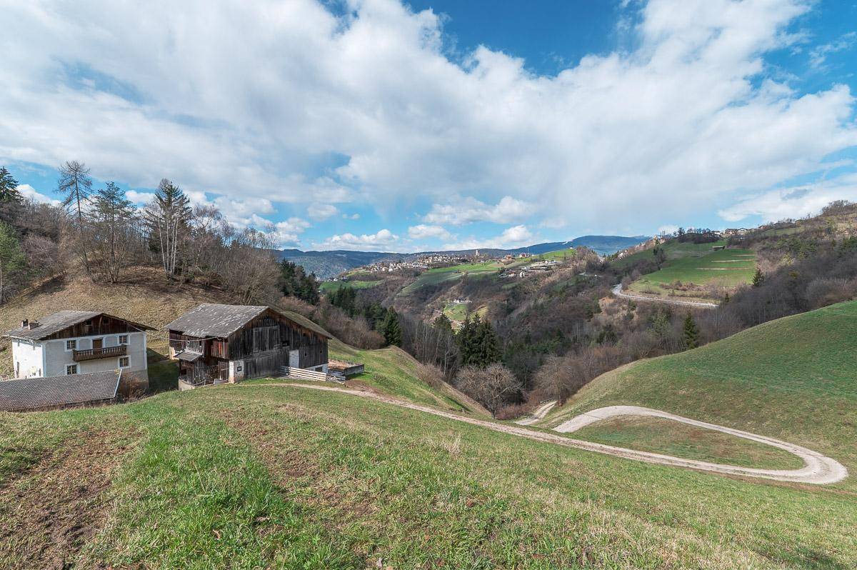 Malerische Hügellandschaft mit zwei Gebäuden, einem Feldweg und einem weiten Blick unter blauem Himmel.
