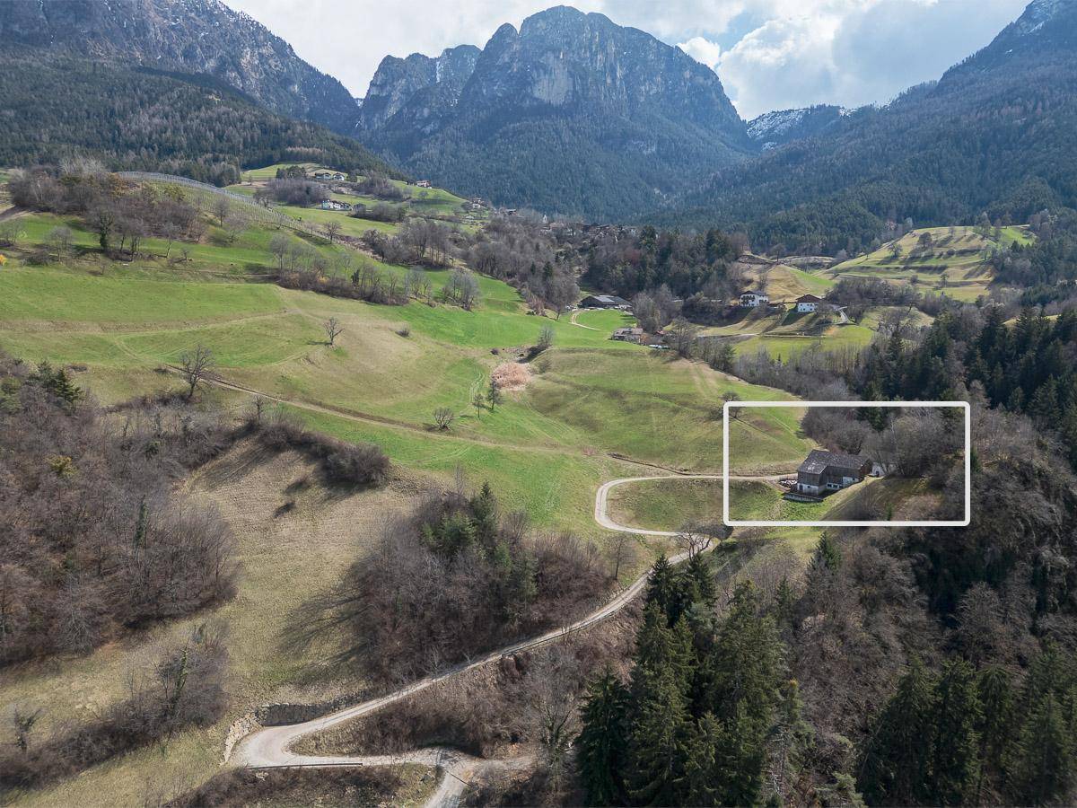 Luftaufnahme einer Berglandschaft mit grünen Hügeln und einem markierten Grundstück mit Gebäuden.