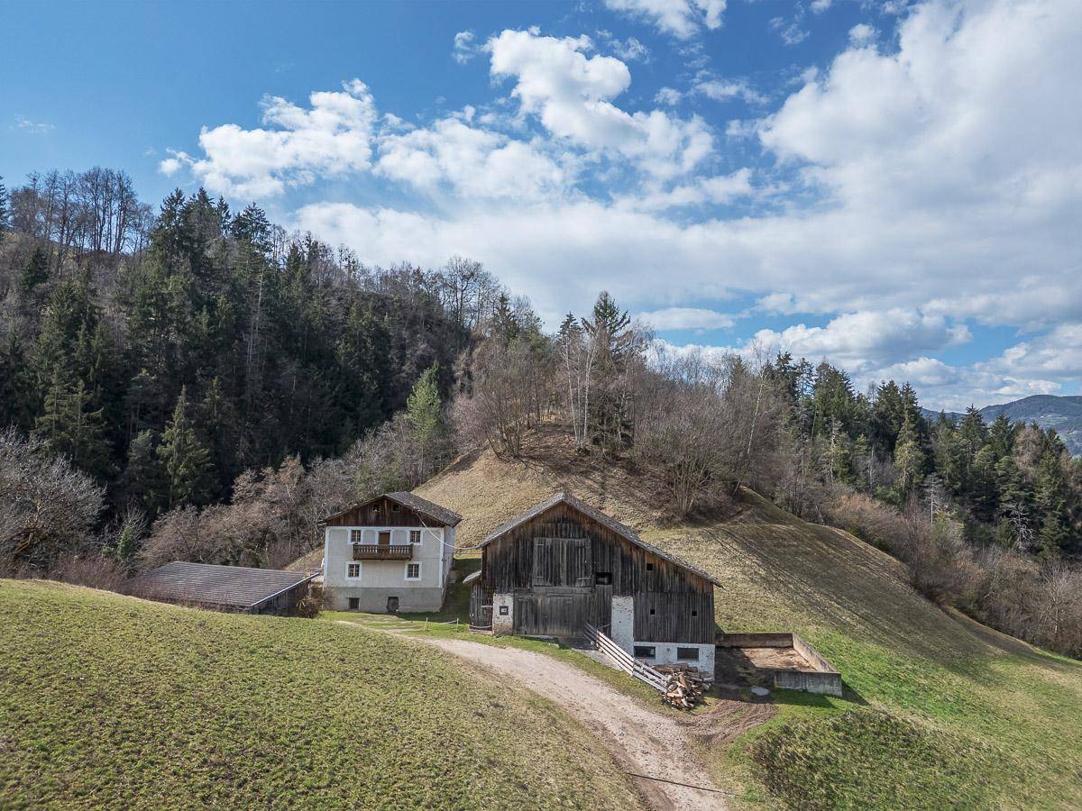 Zwei traditionelle Gebäude auf einem grünen Hügel, umgeben von Bäumen und ländlicher Natur.