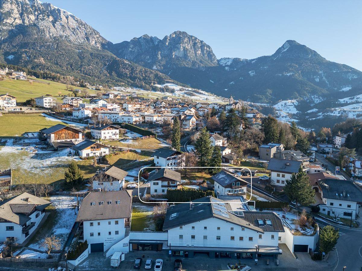 Luftaufnahme eines Dorfes in den Bergen mit schneebedeckten Dächern und umrandetem Grundstück.