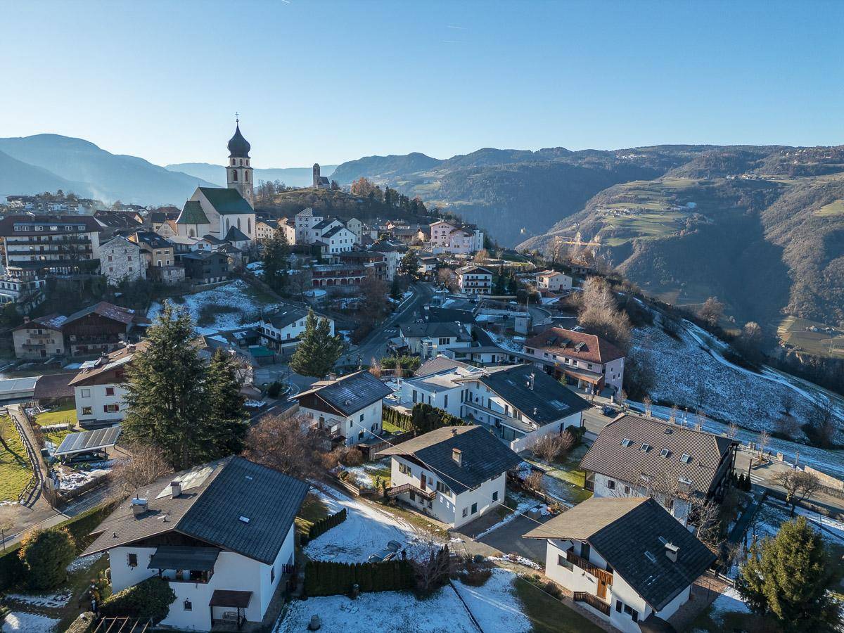Panoramablick auf ein malerisches Dorf mit Kirche und schneebedeckten Bergen im Hintergrund.