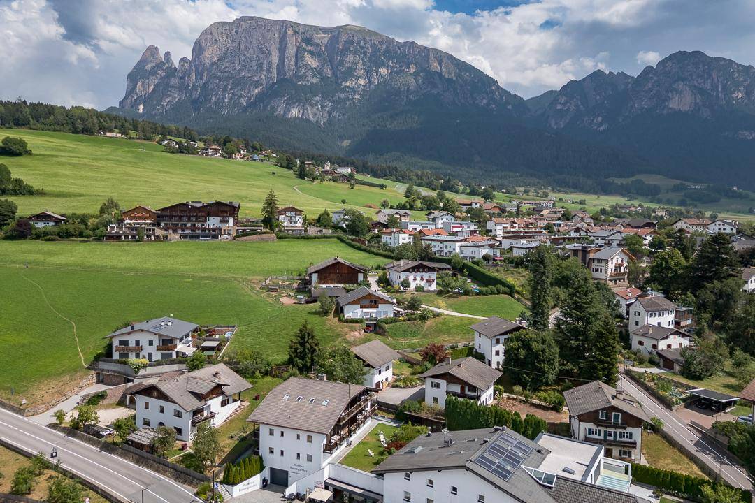 Weitläufige Ansicht eines Bergdorfes mit grünen Wiesen und imposanter Bergkulisse.
