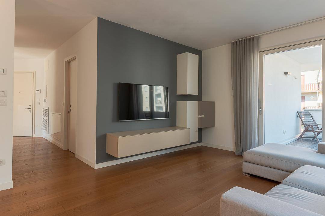 Geräumiges Wohnzimmer mit Holzboden, moderner TV-Wand und Zugang zum Balkon.