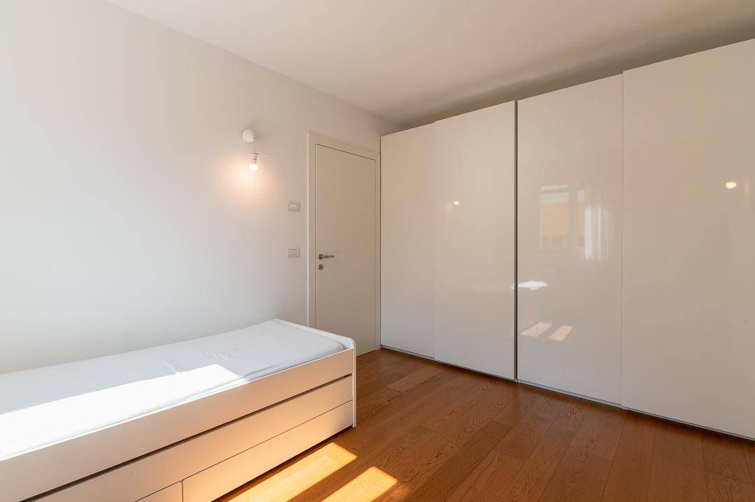 Helles Zimmer mit Einzelbett, großem weißen Kleiderschrank und Holzboden.