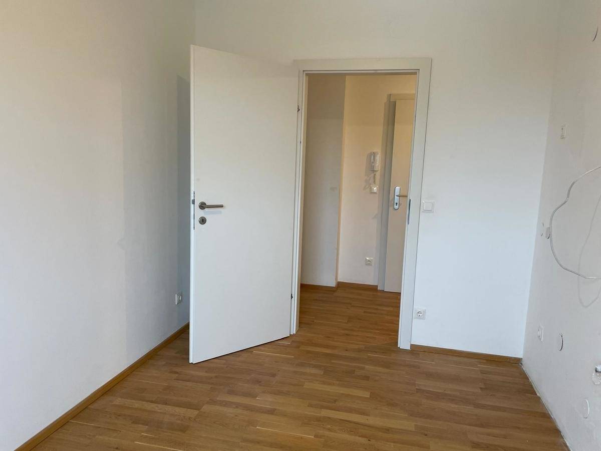 Leeres Zimmer mit Parkettboden und offener Tür zu einem angrenzenden Bereich, hell und sauber.