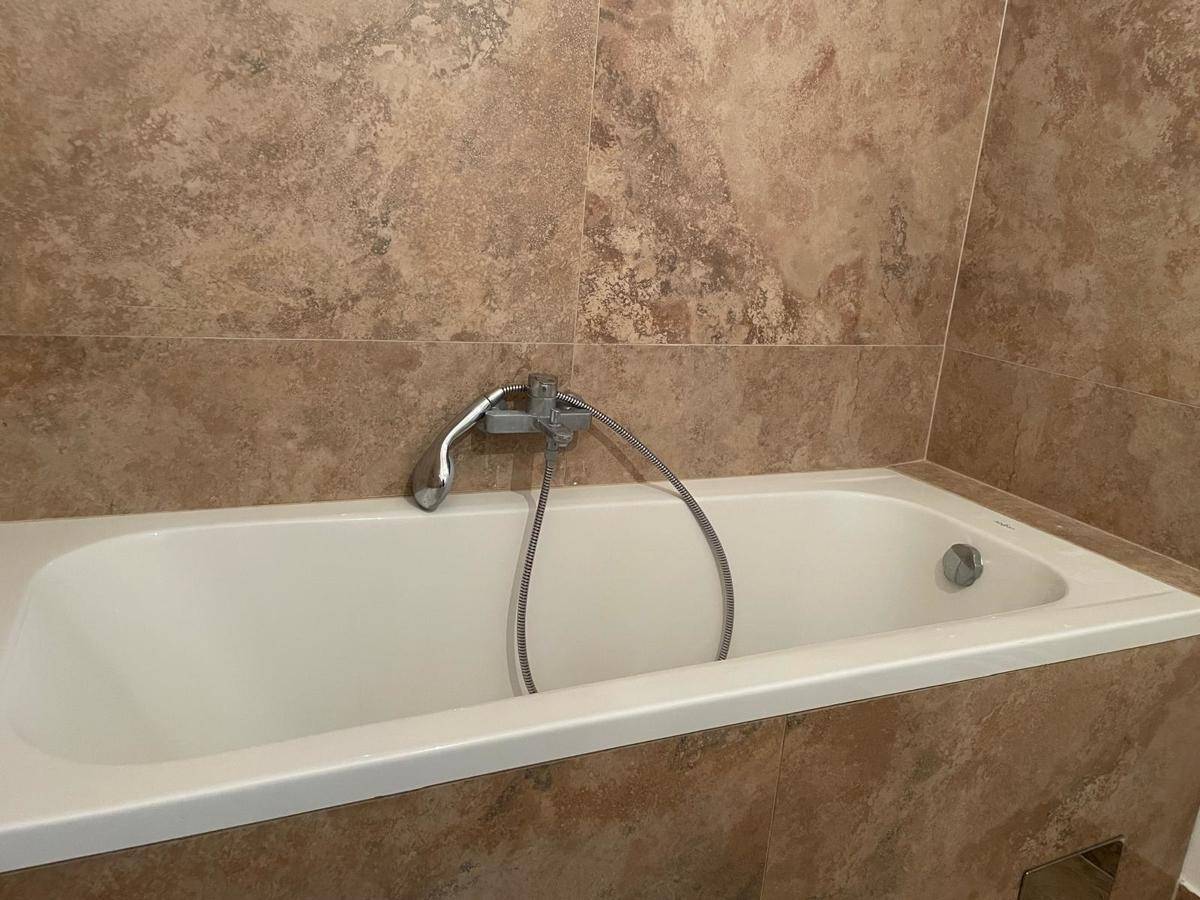 Eingebaute Badewanne mit Duscharmatur in einem gefliesten Badezimmer, praktisch und pflegeleicht.