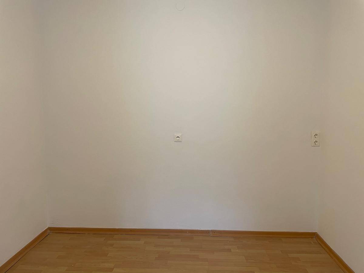 Weiße Wand mit Steckdosen und hellem Parkettboden in einem leeren Raum.