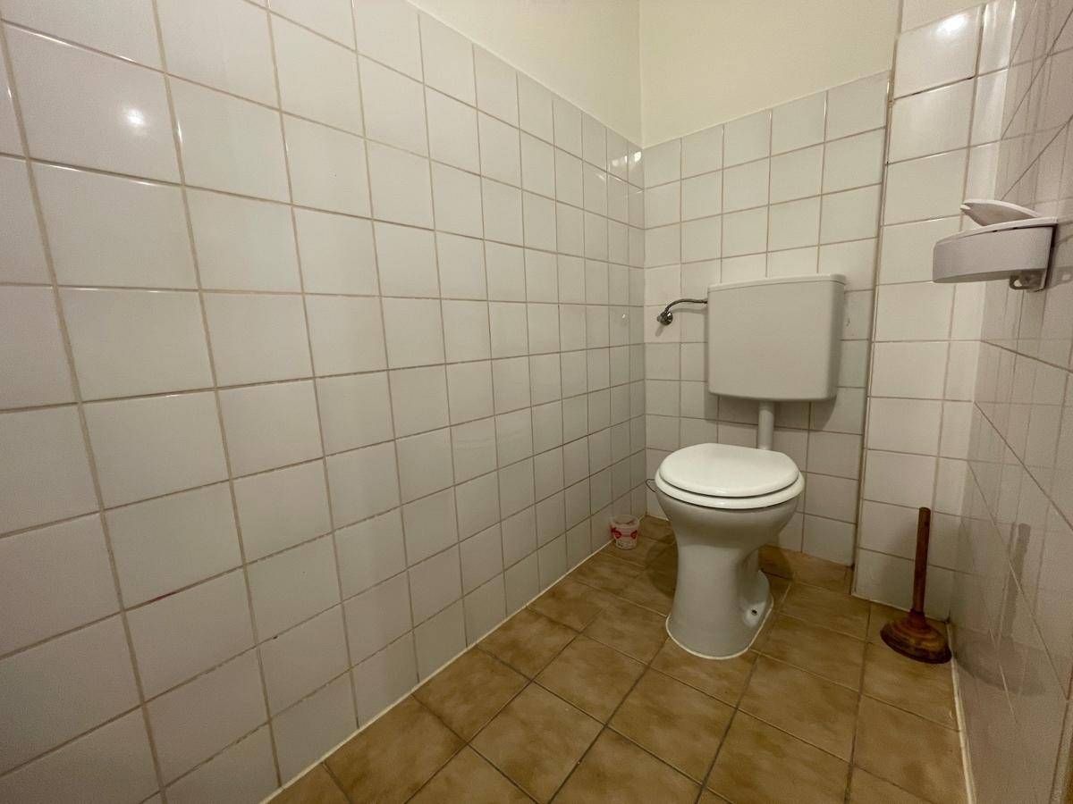 Einfaches WC mit weißen Fliesen an den Wänden und braunem Fliesenboden.