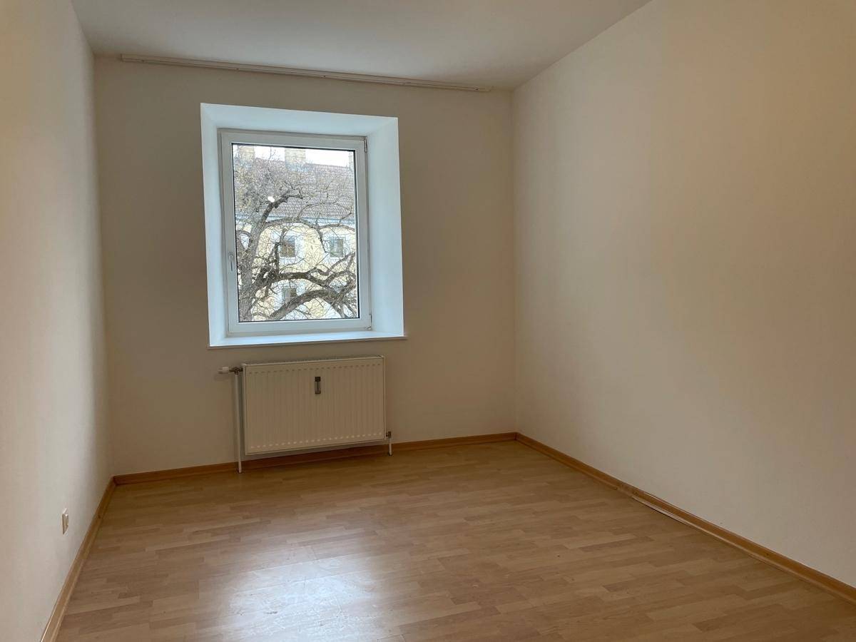 Helles Zimmer mit Parkettboden und einem großen Fenster, das viel Tageslicht hereinlässt.