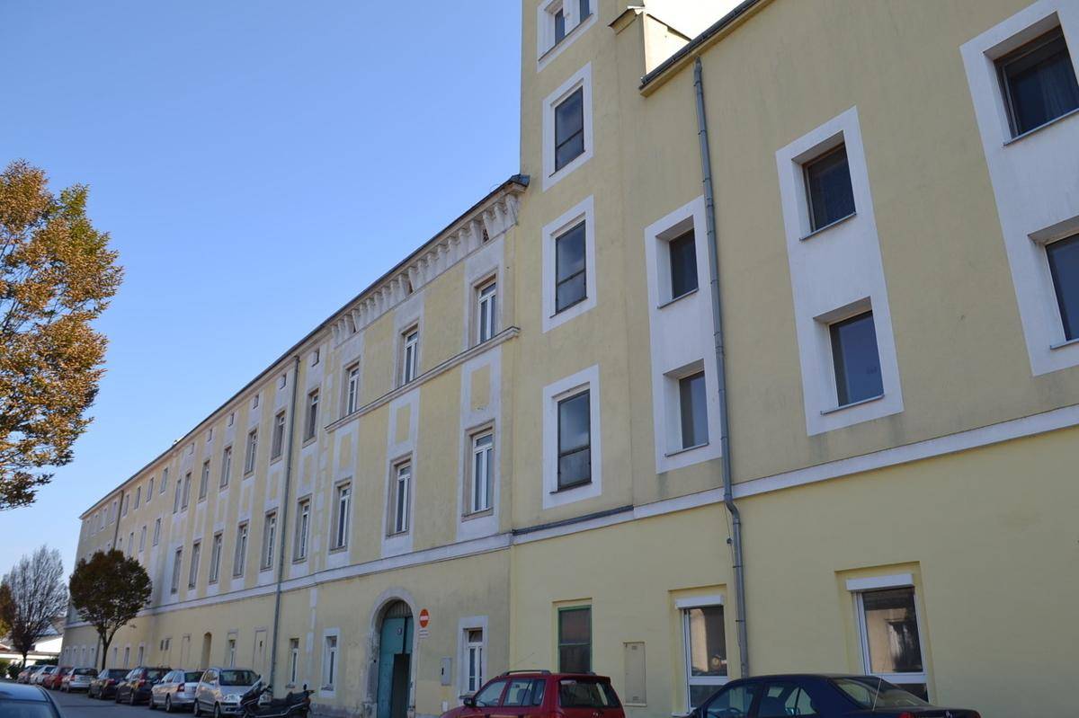 Lange Fassade eines gelben Gebäudes mit vielen Fenstern und parkenden Autos davor.