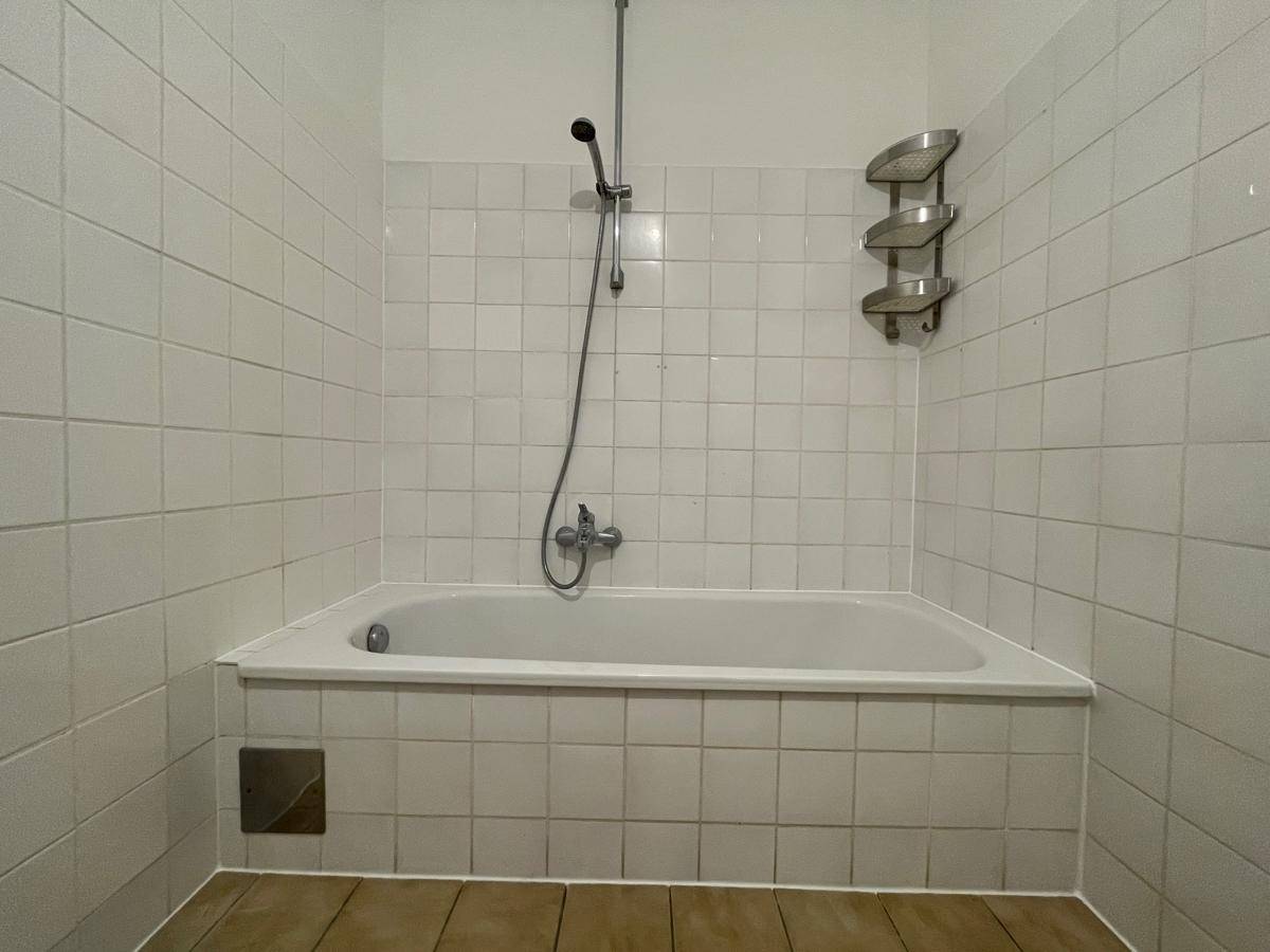 Eingebaute Badewanne mit Duscharmatur und weißen Wandfliesen.