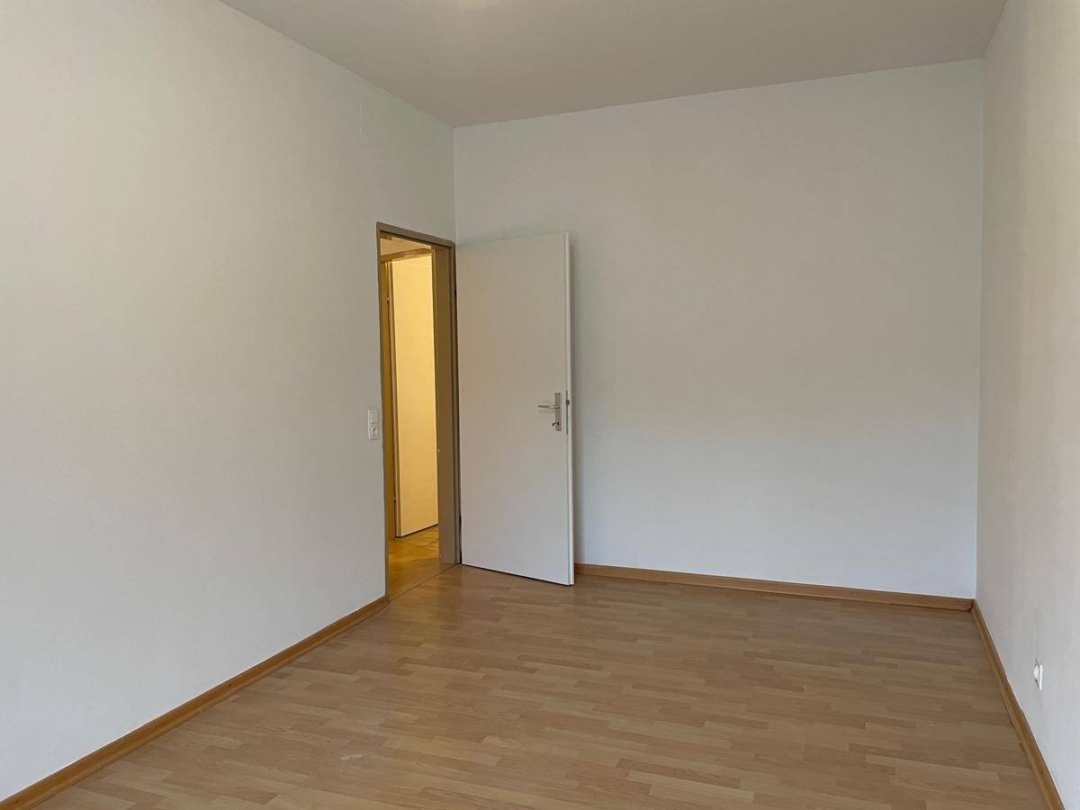 Helles, unmöbliertes Zimmer mit Parkettboden und weiß gestrichenen Wänden.