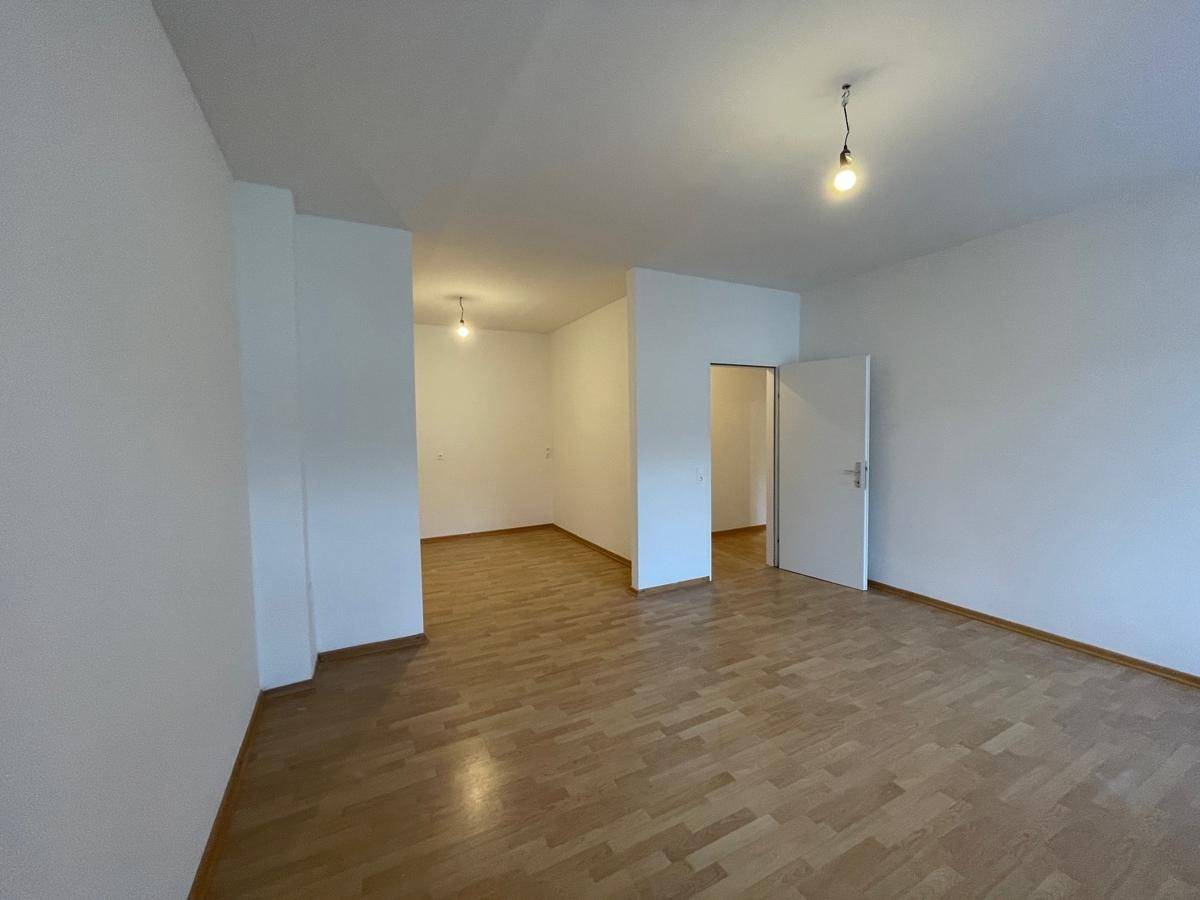 Leeres Zimmer mit Parkettboden und Zugang zu weiteren Räumen.