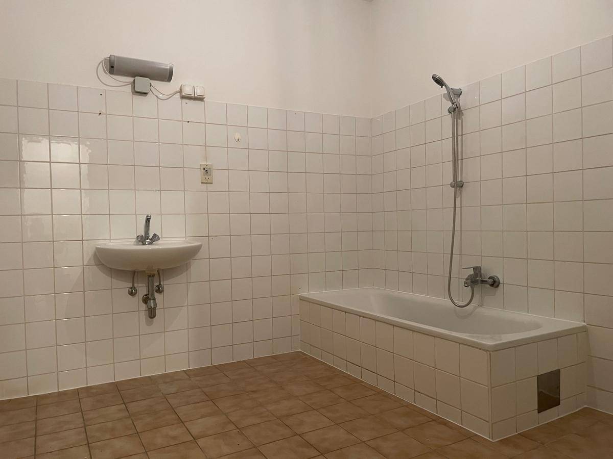 Badezimmer mit Badewanne, Waschbecken und weißen Fliesen, bietet grundlegende Ausstattung.