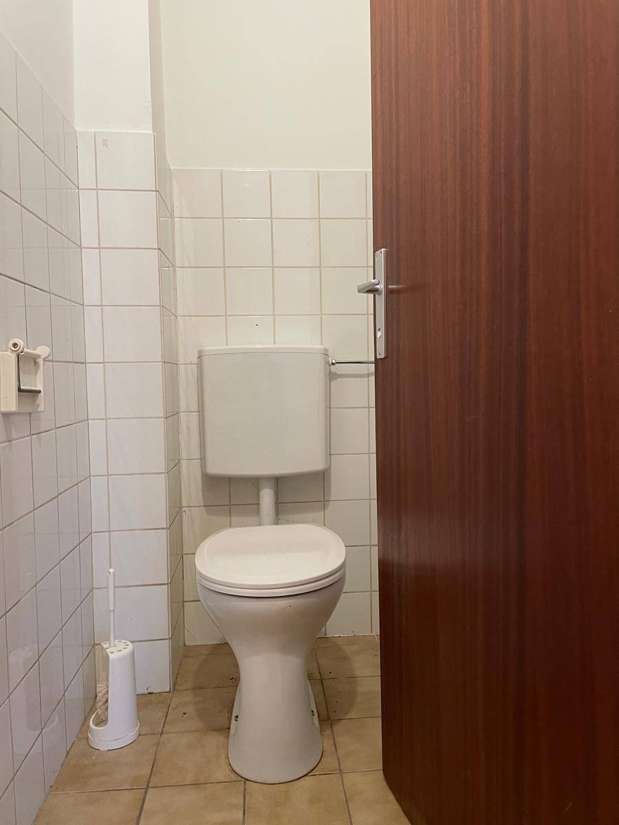 Einfaches WC mit weißen Wandfliesen und Steh-WC, funktional und sauber gehalten.