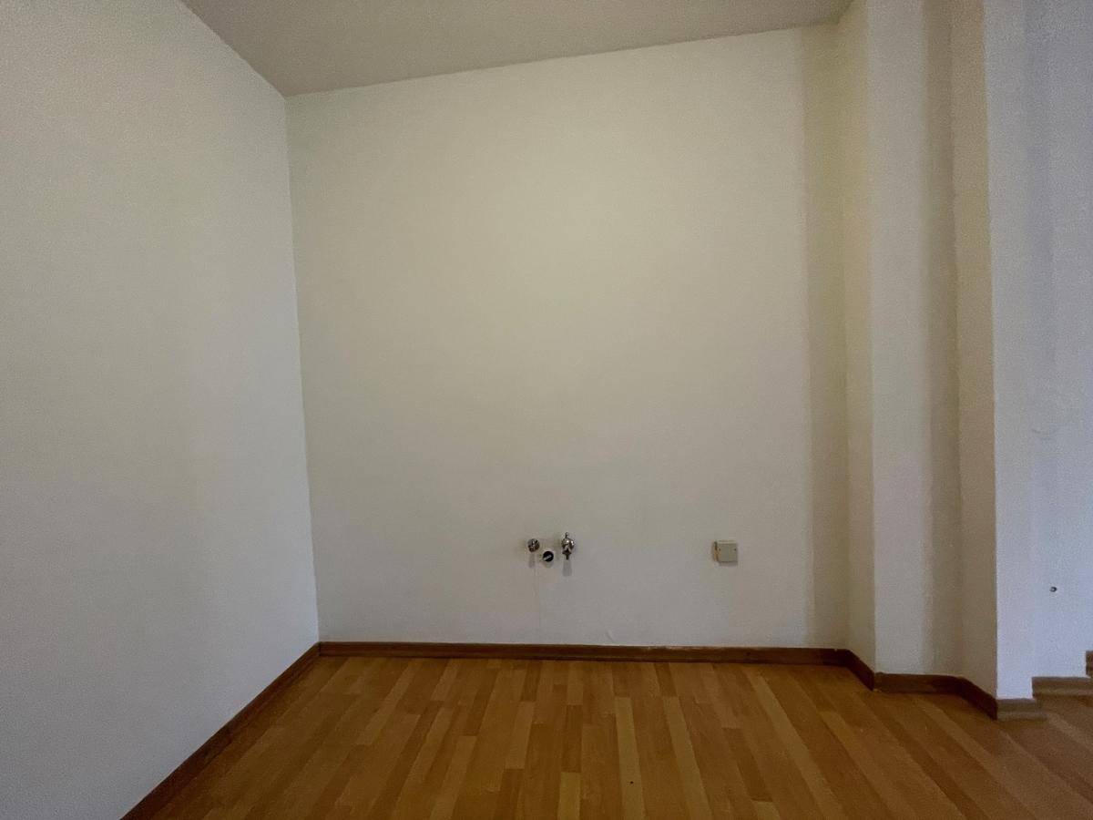 Leerer Raum mit Parkettboden und Anschlüssen für eine Küche, bereit für die Installation.