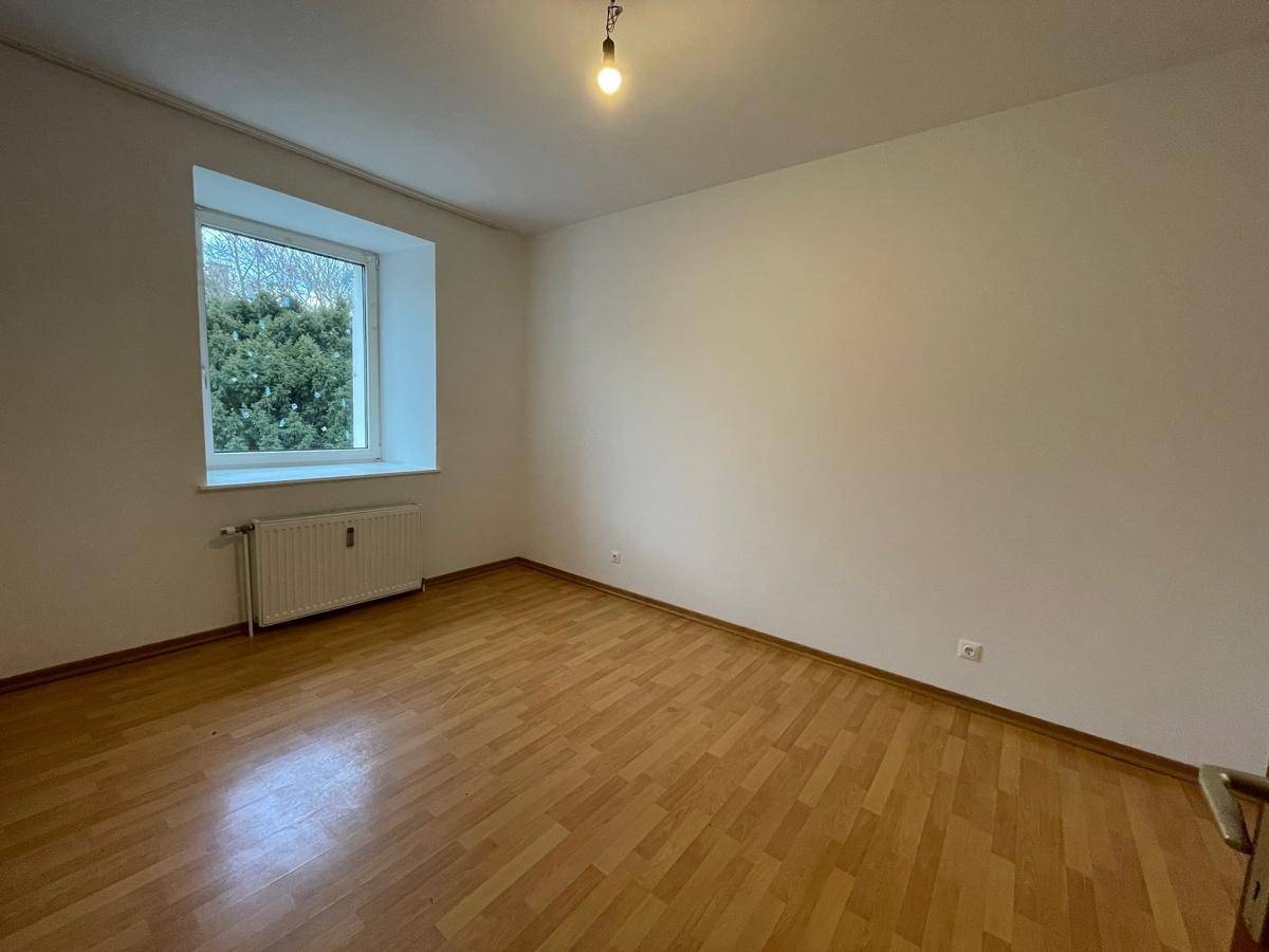 Helles Zimmer mit Parkettboden und Fenster mit Blick ins Grüne, bietet eine ruhige Atmosphäre.