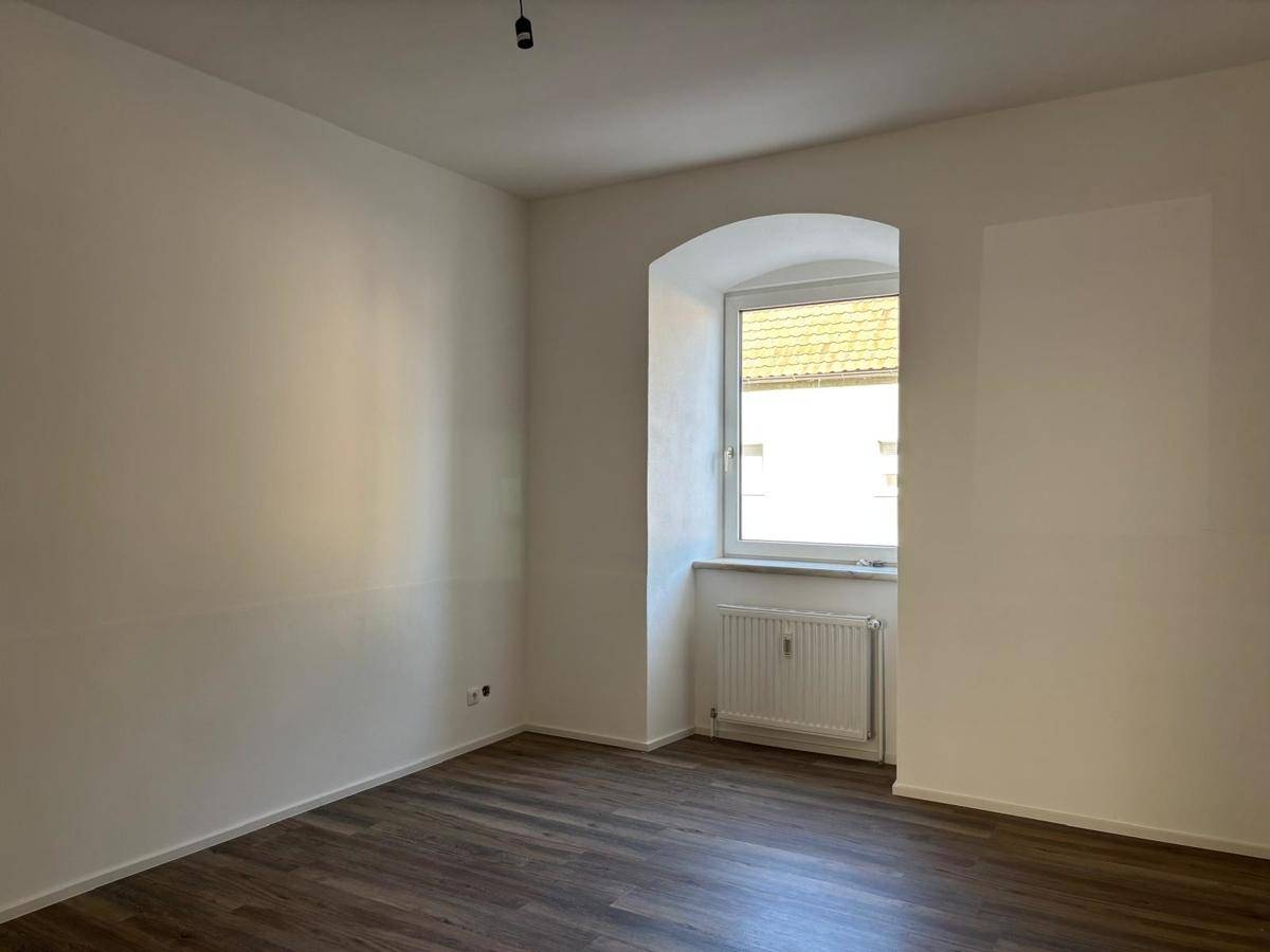 Geräumiges Zimmer mit dunklem Laminatboden und einem charmanten Bogenfenster.