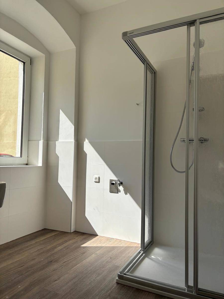 Modernes Badezimmer mit Duschkabine, weißen Fliesen und einem Fenster für Tageslicht.