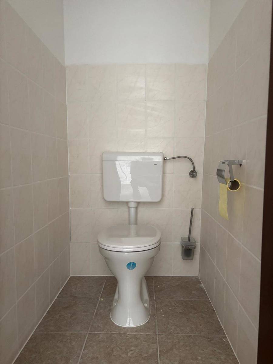 Separates WC mit Toilette und hellen Fliesen an Wänden und Boden.