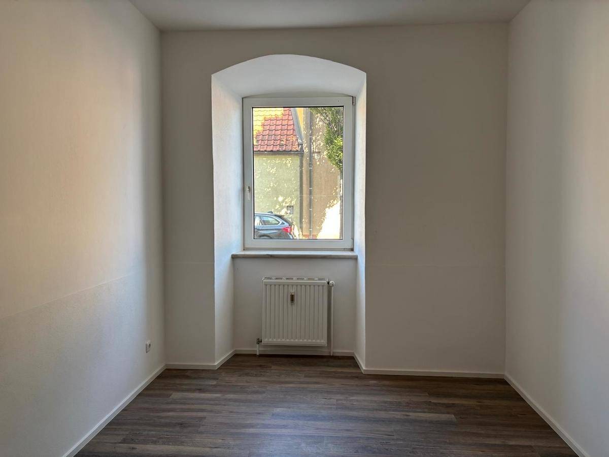 Leeres Zimmer mit Laminatboden und einem Bogenfenster, das auf die Straße blickt.