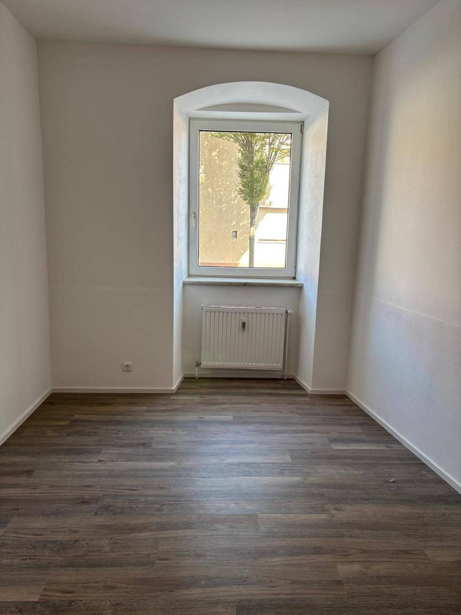 Heller Raum mit Laminatboden und einem Bogenfenster, das einen Blick ins Grüne bietet.