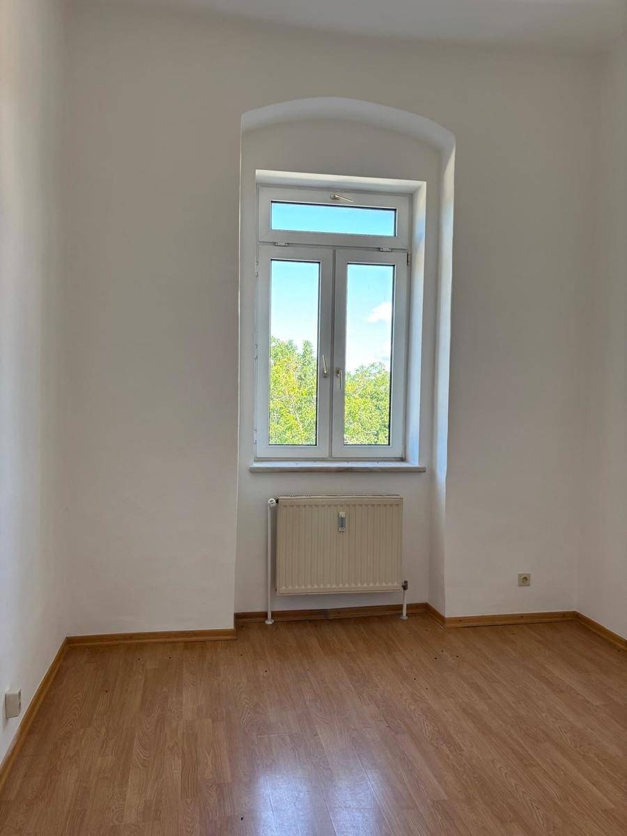 Heller Wohnraum mit Laminatboden und einem großen Fenster, das viel natürliches Licht bietet.