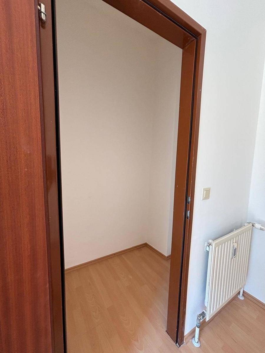 Offene Tür in einem hellen Raum mit Laminatboden, der einen Einblick in einen kleinen Nebenraum gewährt.