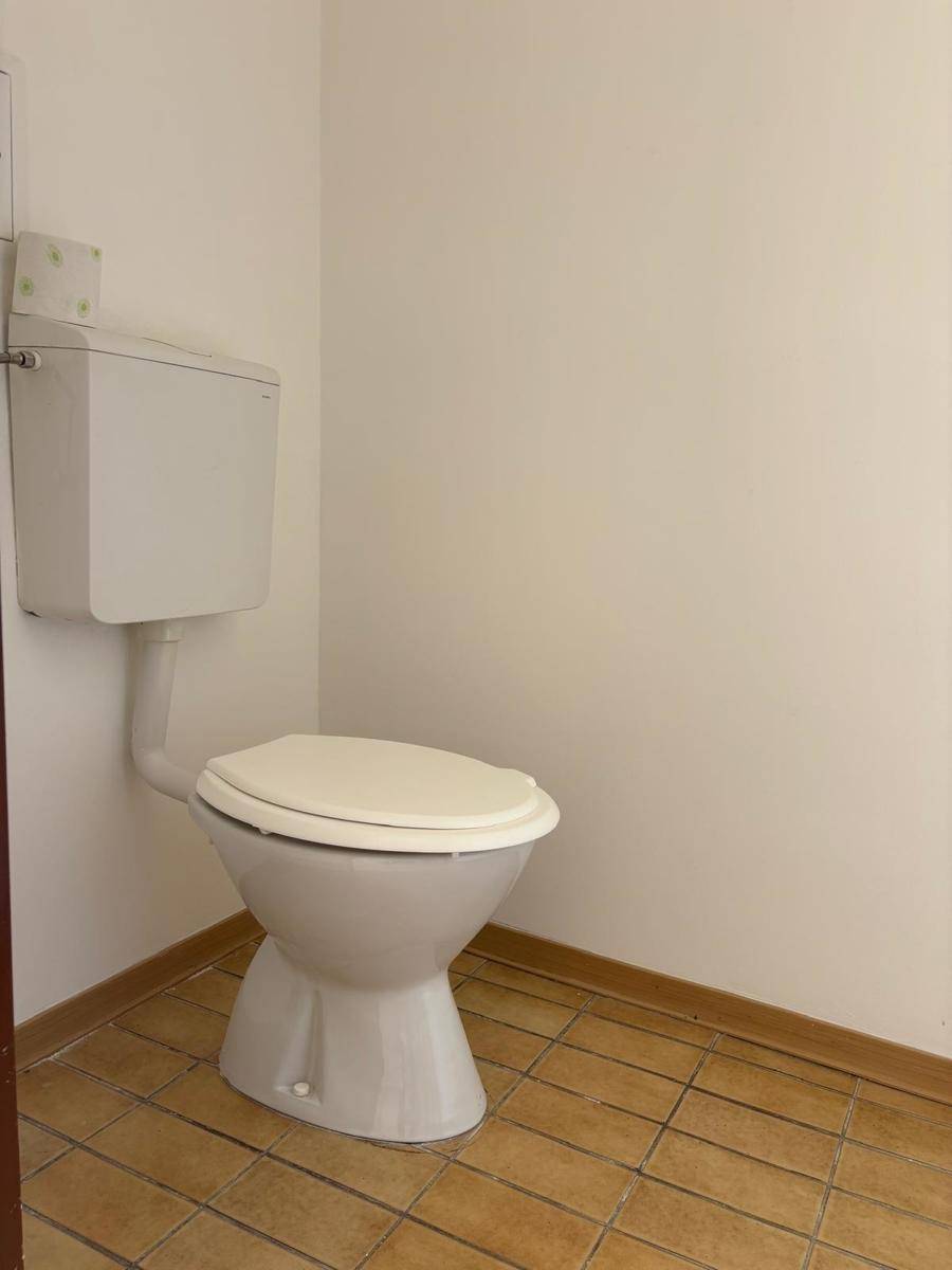 Einfache Toilette mit Fliesenboden und einem Spülkasten, funktional und sauber gehalten.