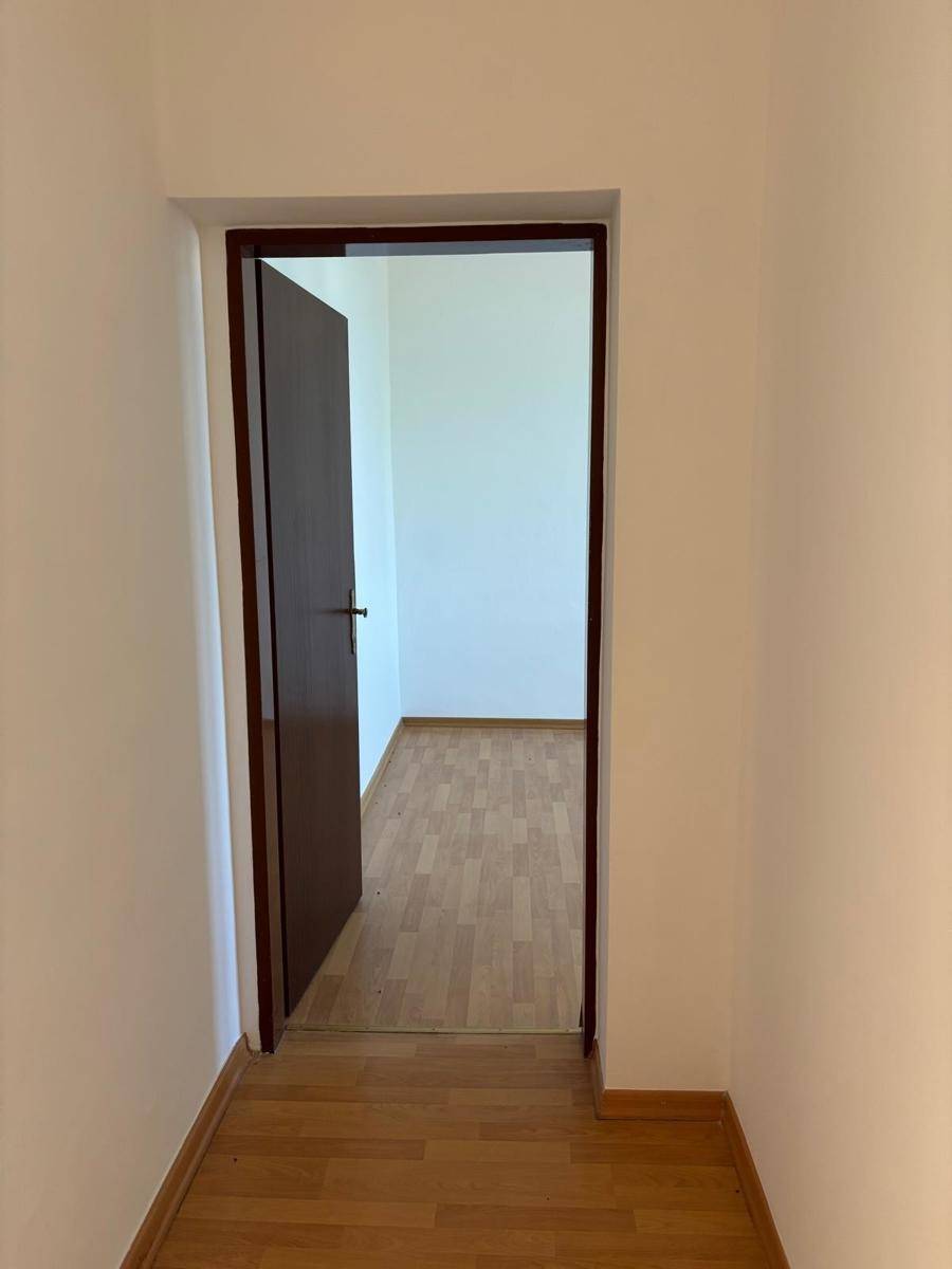 Offene Tür in einem hellen Raum mit Laminatboden, der zu einem weiteren Zimmer führt.