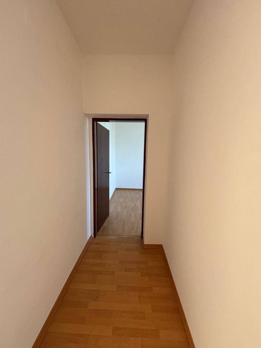 Schmaler Flur mit Laminatboden und einer offenen Tür, die den Blick in einen weiteren Raum freigibt.