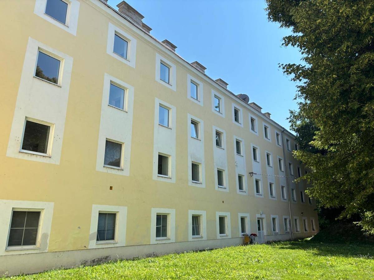 Lange Fassade eines gelben Gebäudes mit vielen Fenstern und einer gepflegten Grünfläche davor.