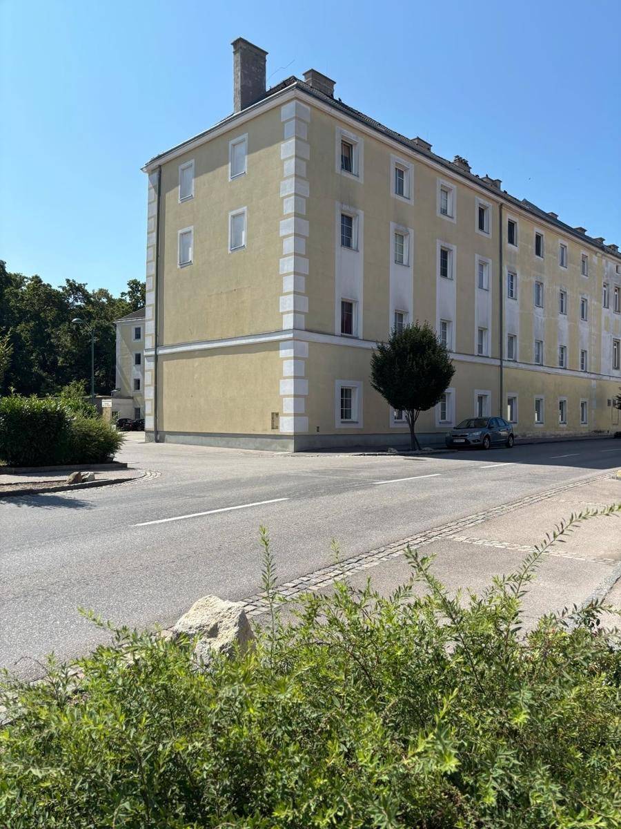 Eckansicht eines großen, gelben Gebäudes mit vielen Fenstern und einer ruhigen Straße davor.
