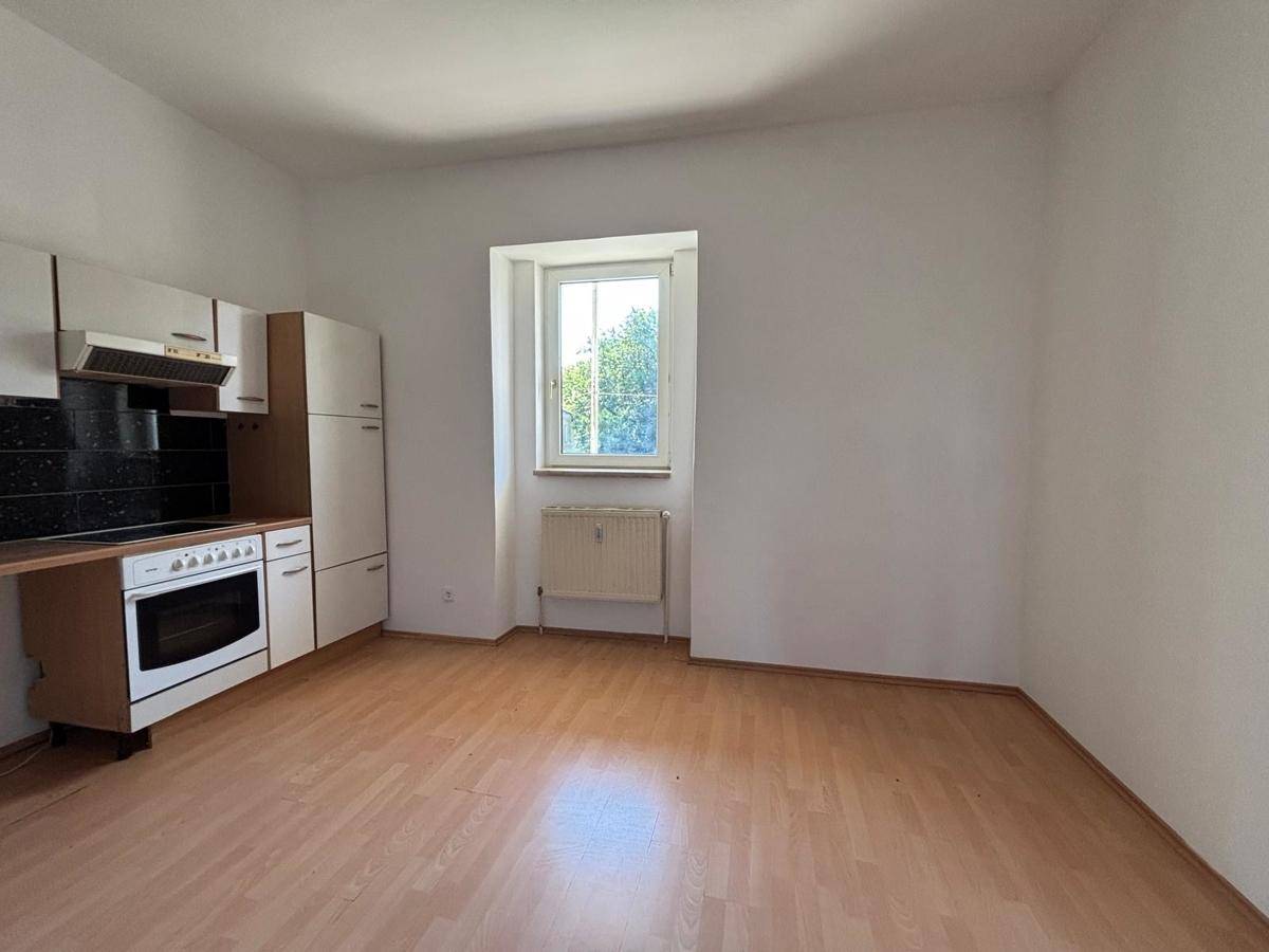 Heller Raum mit einfacher Küchenzeile, Fenster und Laminatboden, bereit zur individuellen Gestaltung.