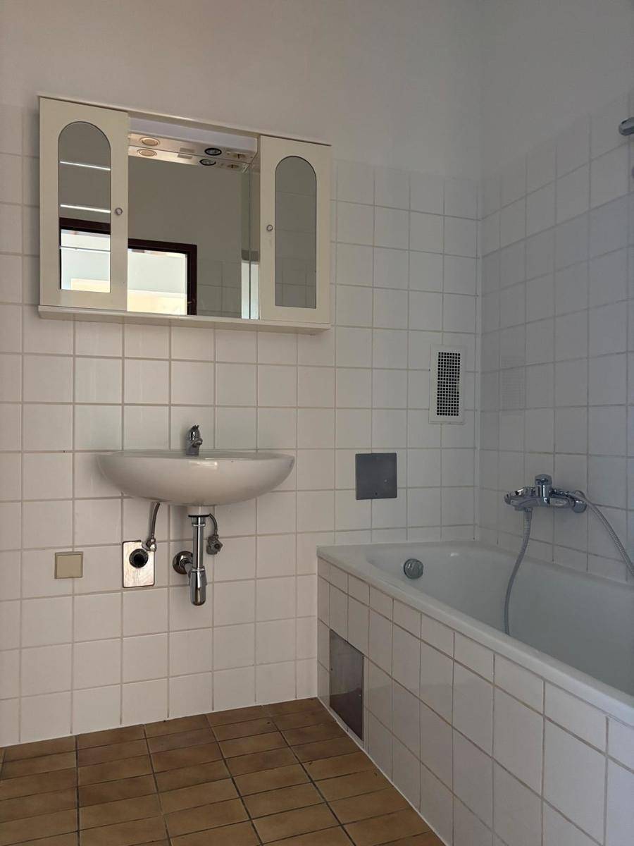 Badezimmer mit Badewanne, Waschbecken und weißen Fliesen, ausgestattet mit einem praktischen Spiegelschrank.