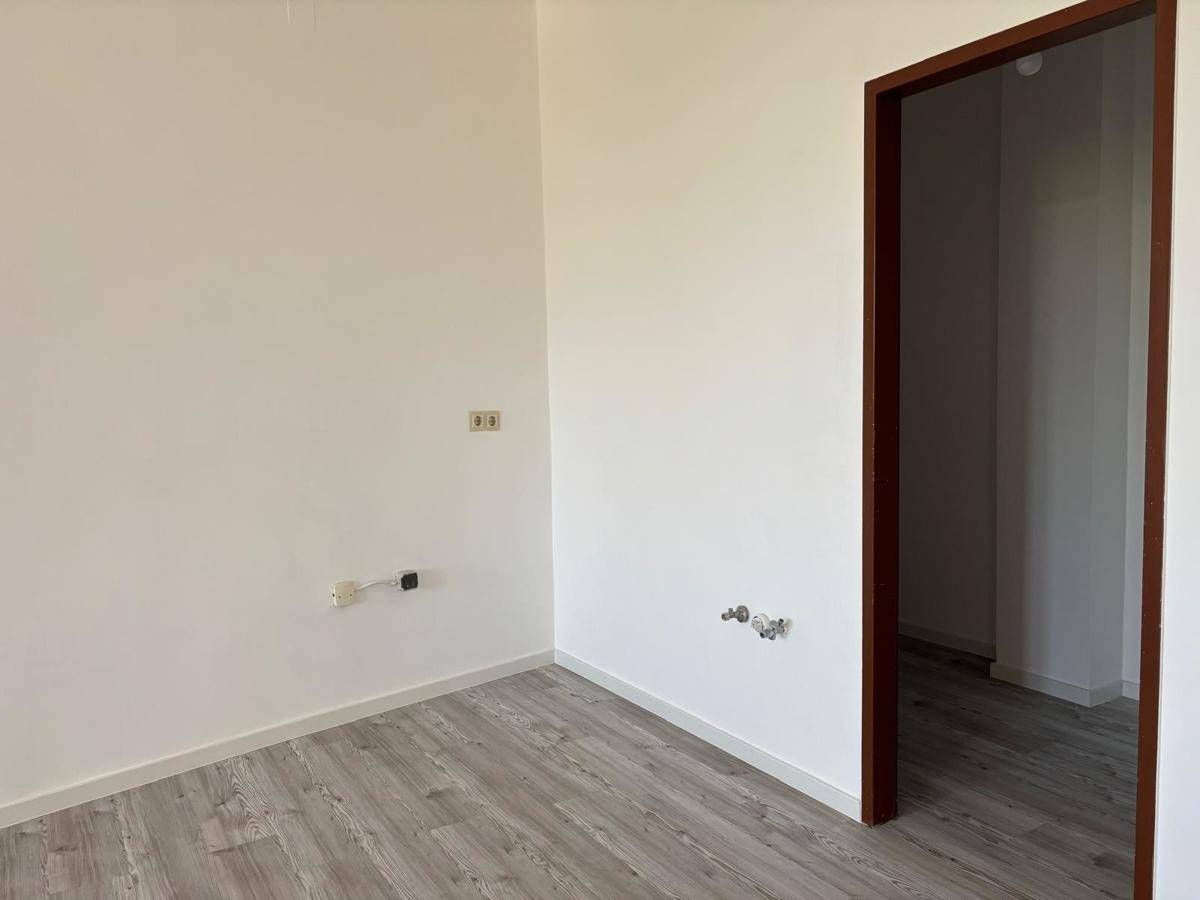 Leerer Raum, vorbereitet für eine Küche, mit Anschlüssen an der Wand und hellem Laminatboden.