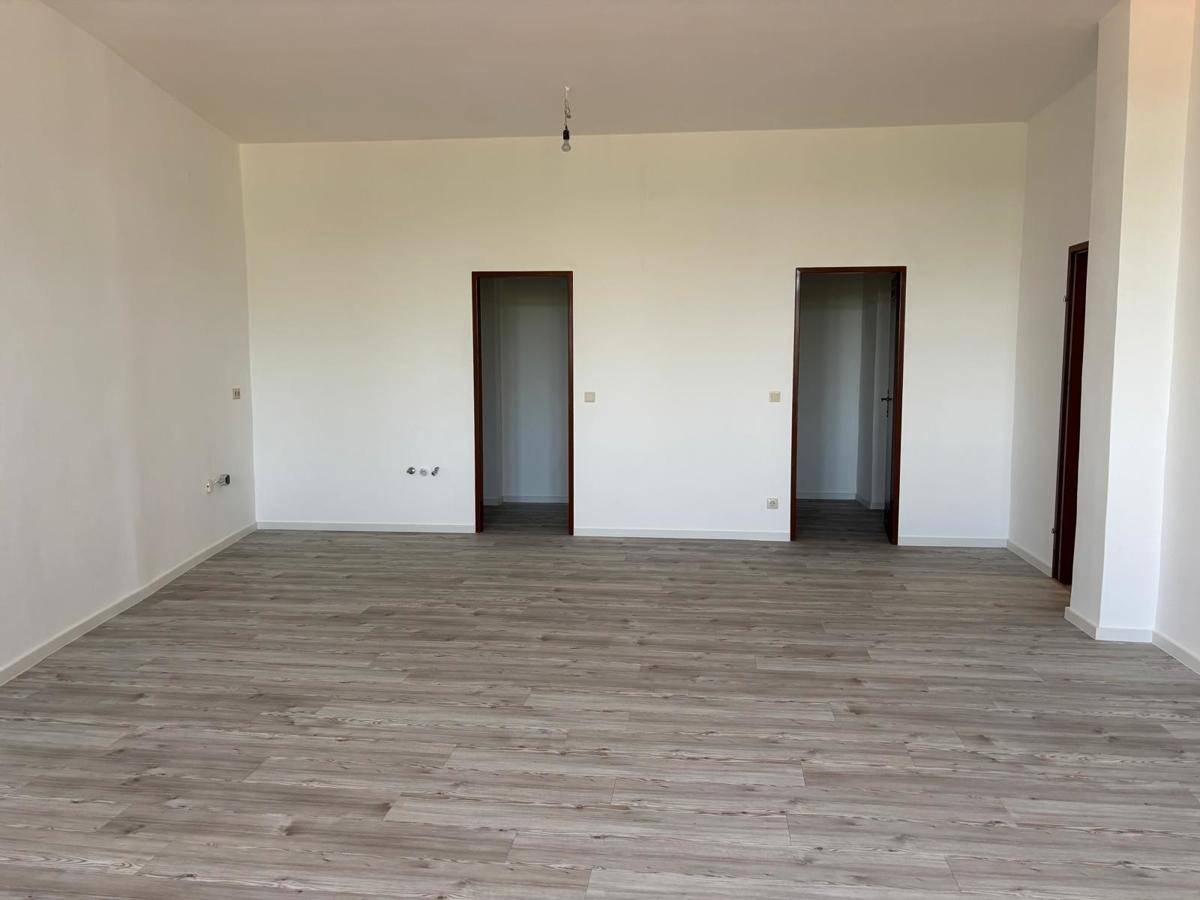 Leeres Zimmer mit hellem Laminatboden und zwei Türen, die zu weiteren Räumen führen.