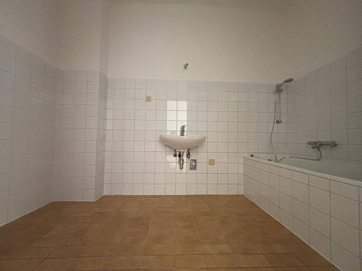Badezimmer mit weißen Fliesen, einer Badewanne und einem Waschbecken, in gutem Zustand.