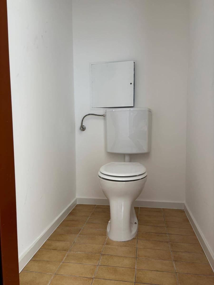 Separate Toilette mit Steh-WC und braunen Bodenfliesen, in einem einfachen, sauberen Zustand.
