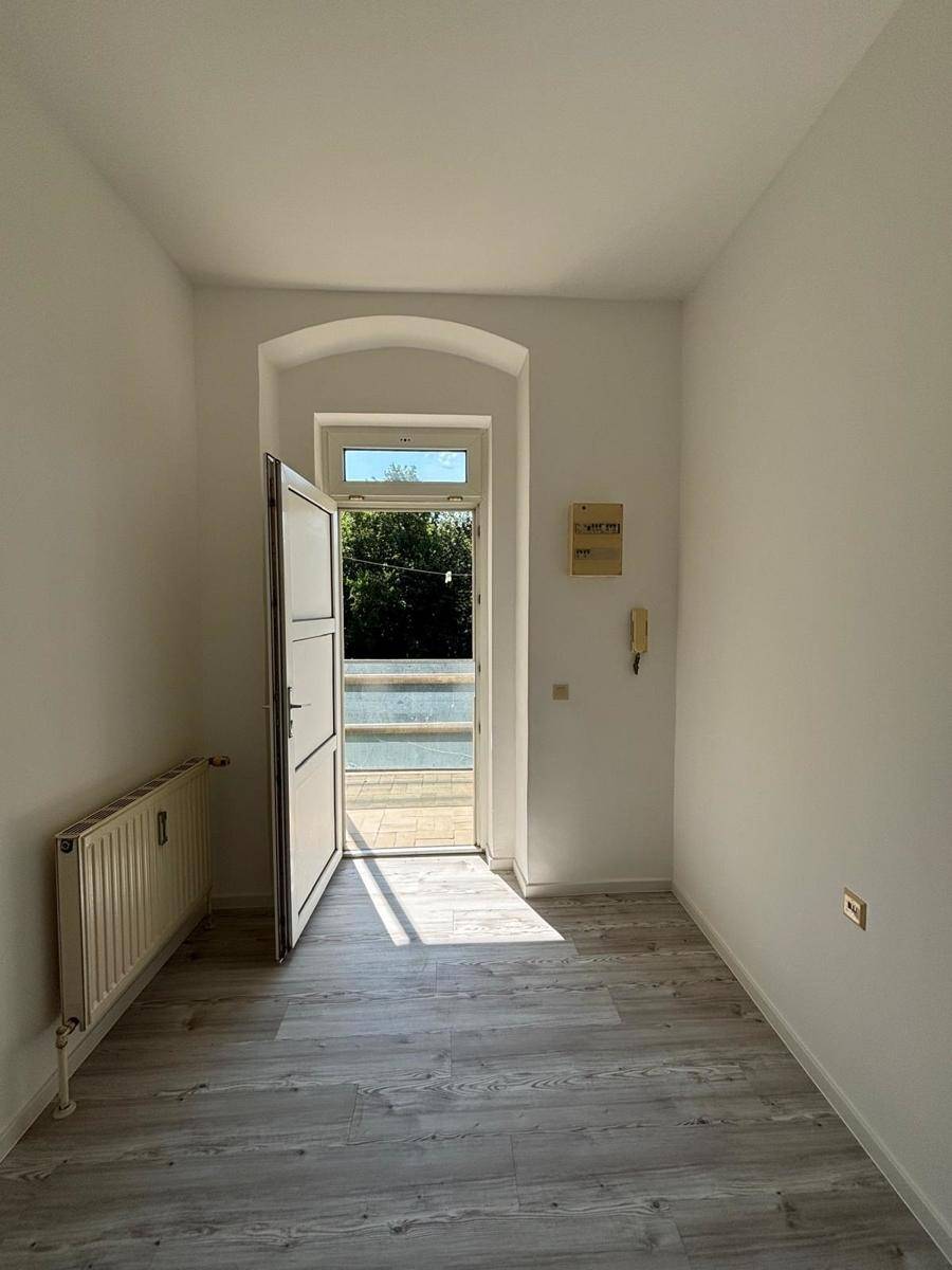 Heller Eingangsbereich mit Zugang zu einem Außenbereich und einem Heizkörper unter dem Fenster.