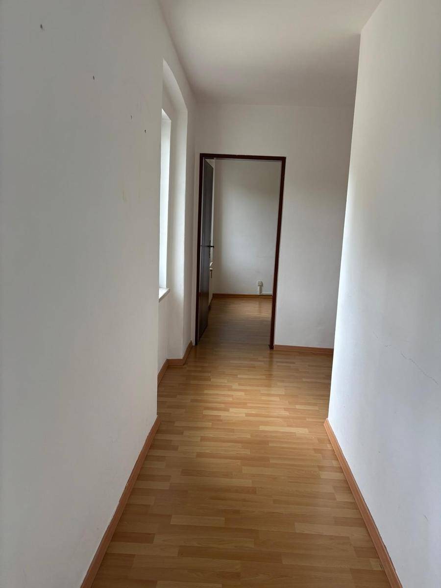 Heller Flur mit Laminatboden und weiß gestrichenen Wänden, der einen Durchgang zu einem Zimmer bietet.