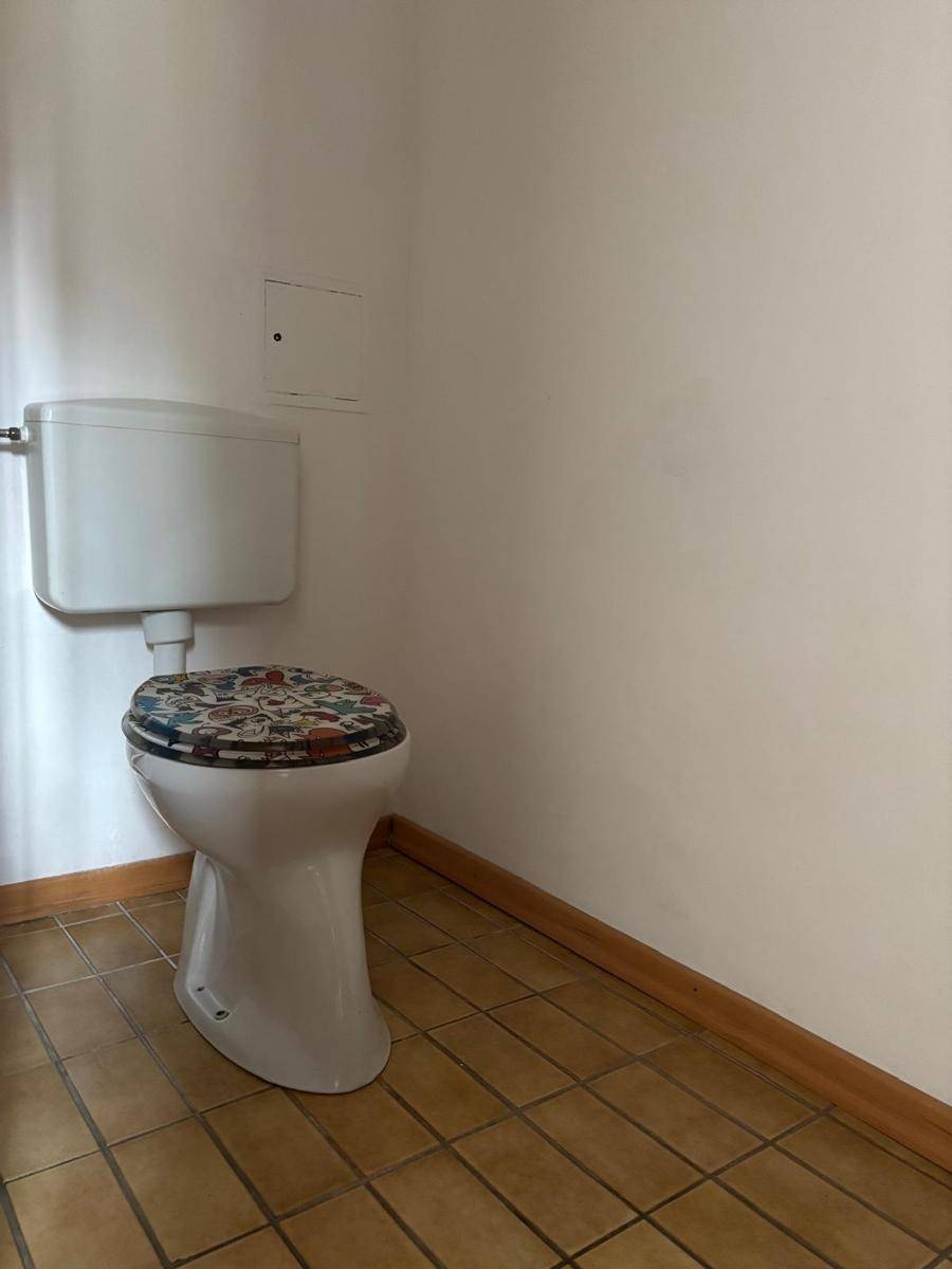 Separates WC mit Steh-WC und braunen Bodenfliesen, ausgestattet mit einem farbigen Toilettensitz.