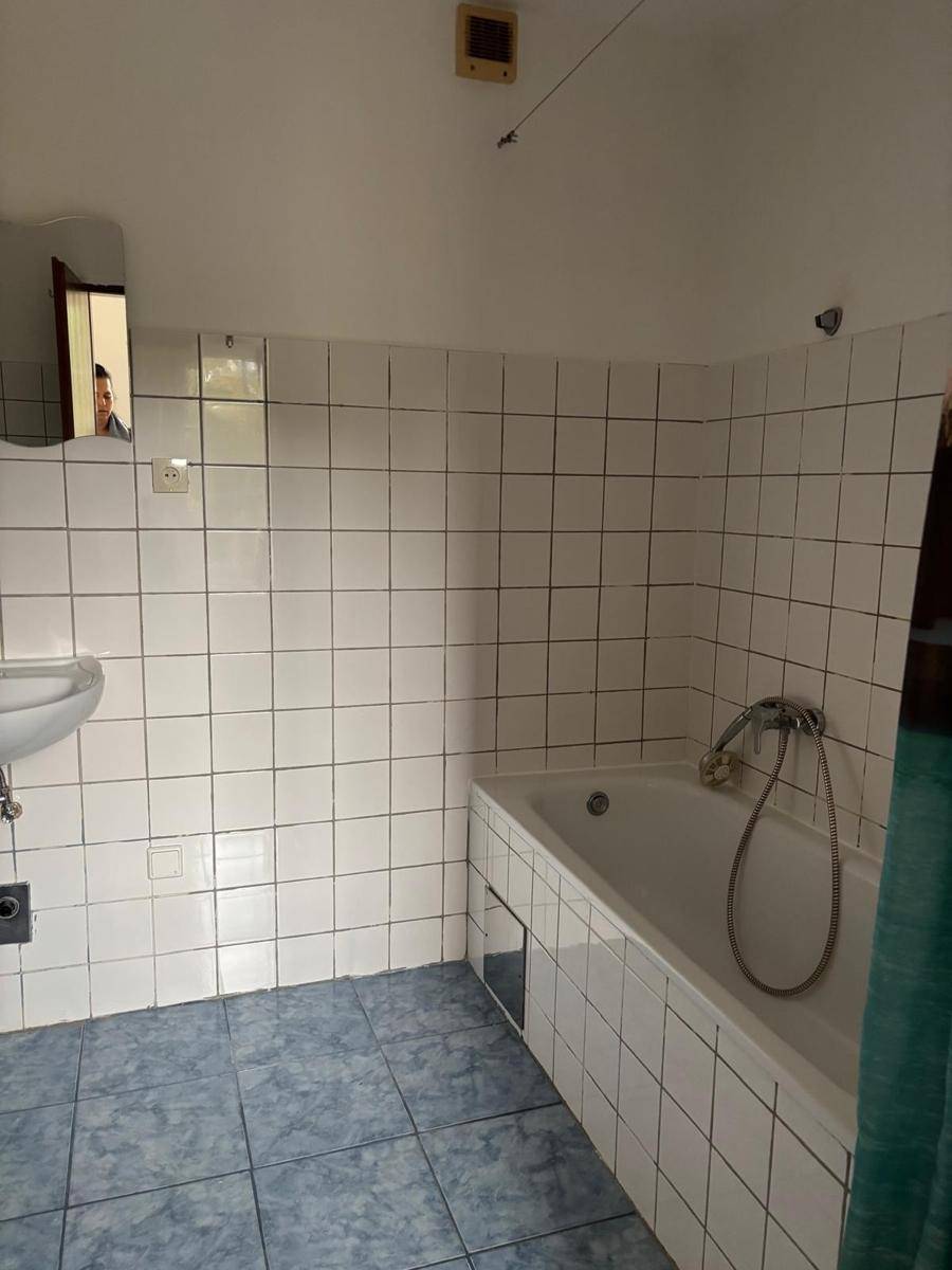 Badezimmer mit weißen Wandfliesen, blauen Bodenfliesen, Badewanne und Waschbecken.