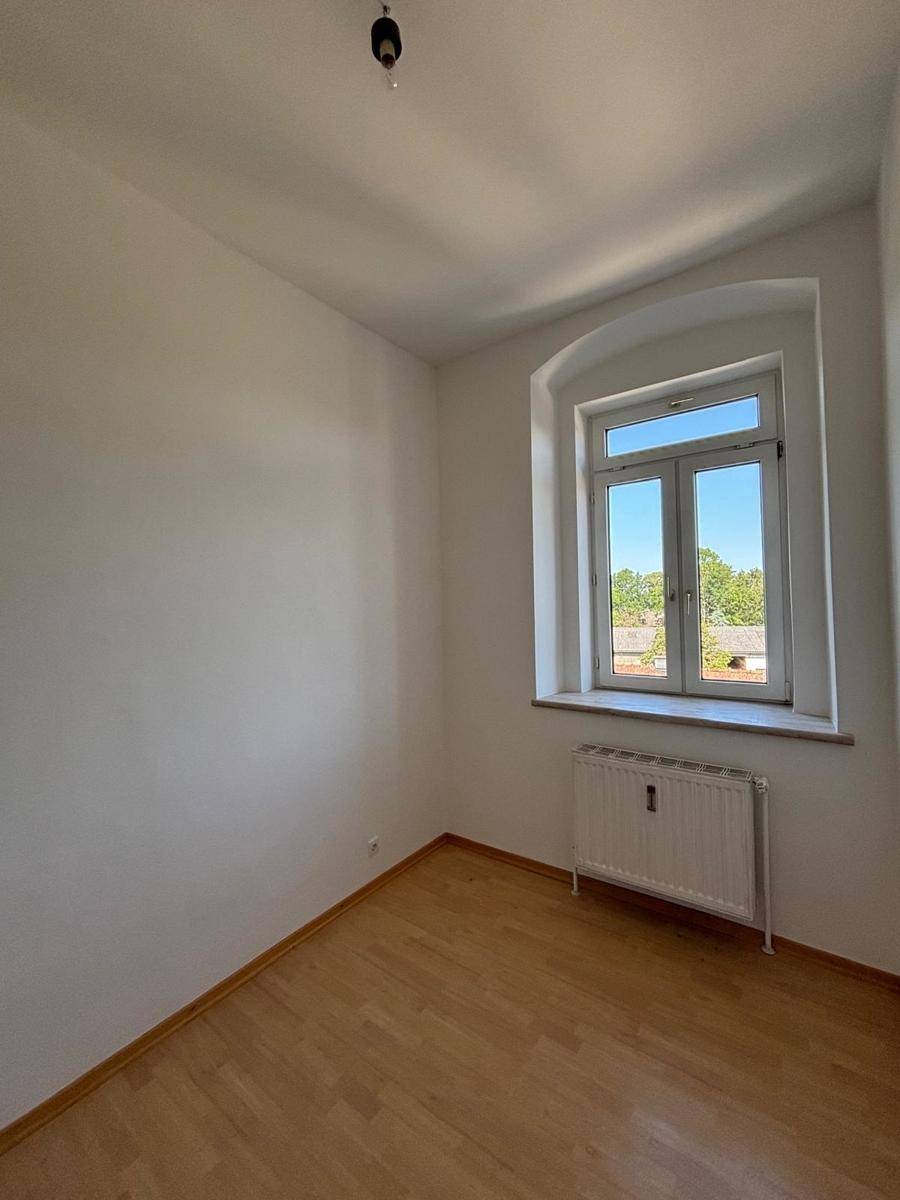 Kleineres Zimmer mit Holzfußboden, Fenster und Heizkörper, ideal als Schlaf- oder Arbeitszimmer.